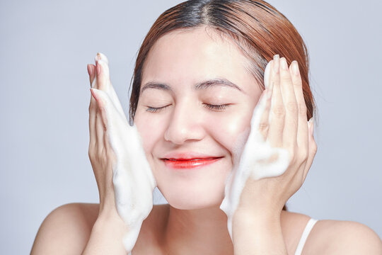 Smiling young woman washing foam face by natural foamy gel. satisfied girl with bare shoulders applying cleansing beauty product on cheeks. personal hygiene, skincare daily routine.