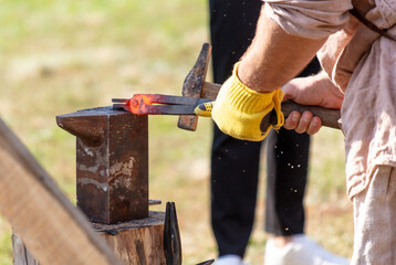 A blacksmith forges metal with a hammer on an anvil in the park