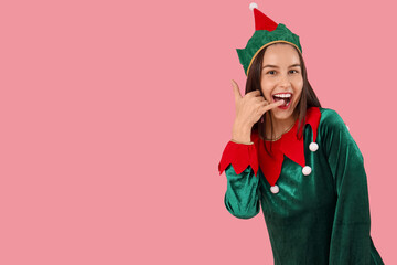 Beautiful young woman in elf's costume showing "call me" gesture on pink background