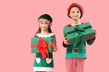 Cute little children in elf's costumes with gift boxes on pink background