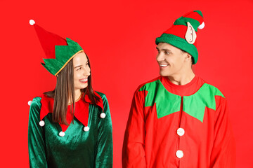 Happy couple in elf's costumes on red background