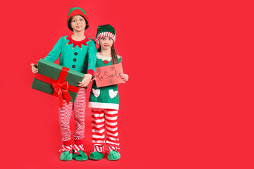 Cute little children in elf's costumes with gift box and card to Santa on red background