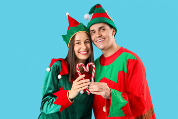 Happy couple in elf's costumes with candy canes on blue background