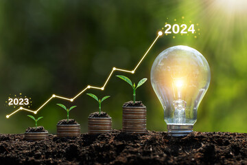 Seedlings are growing on stacked coins in soil with growth compared to year 2023-2024 and light bulb for innovations and ideas for the new year. investment growth. Development to success in year 2024. - obrazy, fototapety, plakaty