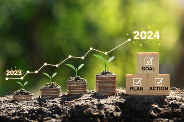 Seedlings are growing on the Coins stack compared to the year 2023-2024 and cubes with text plan, goal, and action. Concept of business growth, profit, and development to succeed in the year 2024.