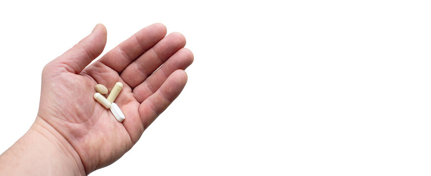 A male hand holds four assorted pills on a white background. Concept of medication, health, and treatment. Ideal for medical and pharmaceutical stock photos.