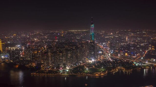 Night hyperlapse of city and landmark skyscraper on waterfront from aerial view. Buildings are illuminated. Traffic can be seen moving along the river, roads and bridges of Ho Chi Minh City, Vietnam.