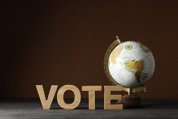 Wooden letters and globe on wooden table on brown background, space for text