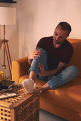 Man with knee pain sitting on a sofa at home.