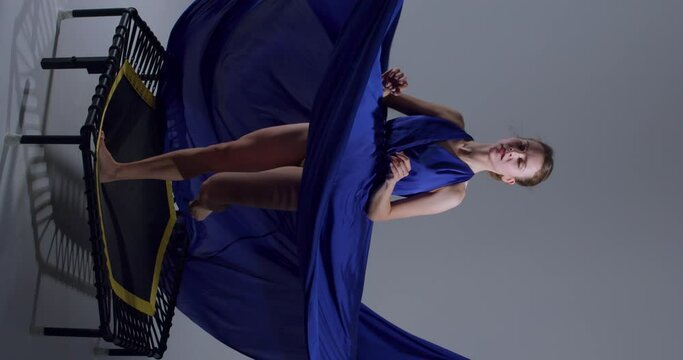 beautiful dancer in long evening blue dress jumping on trampoline, creative art, ballet on air, dancing and sport Slow motion Vertical view lifestyle free spare time, ballet girl has fun in studio