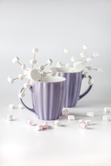 A purple mugs with hot coffee and marshmallows. Two cups with marshmallows in snowflake shapes.