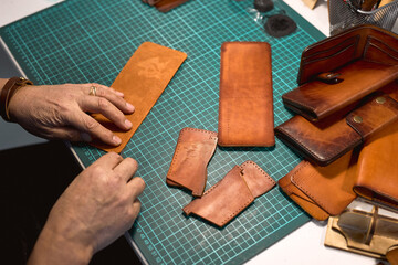 man cutting leather with knife for sewing a wallet. close up cropped shot. Leather work. Tools for sewing bags, wallets, clutches. Sewing products by hand. Manufacture of leather goods.