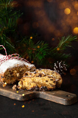 A traditional German fruitcake dusted with powdered sugar beside pine branches and holiday decorations, Christmas stollen dessert at festive bokeh background