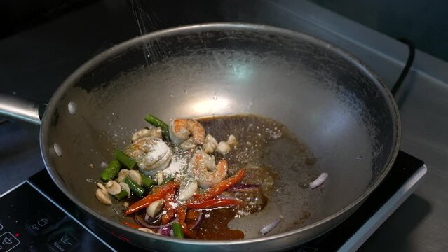 Cooking rice with shrimps with vegetables in a frying pan on a black background from a professional chef. Seafood. Vegetarian, dietary food.