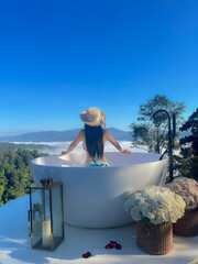 Young woman sitting in the bathtub and looking beautiful views of the fog and mountains.Pretty...