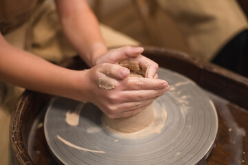 Potter girl works on potter's wheel, making ceramic pot out of clay in pottery workshop. Art and hobby concept