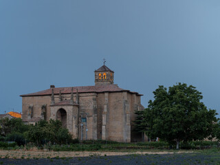 Fototapeta na wymiar Santa Cruz (Holy Cross) church in small village of La Rioja, in the north of Spain. Old church at sunset, with illuminated bell tower