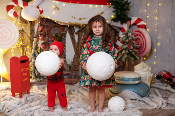 Boy and girl children hold huge snowballs in their hands against the backdrop of a fairy-tale house...