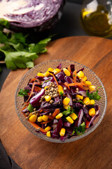  Fresh salad with red cabbage, carrots, hemp seeds and corn in a bowl on the table, vertical photo