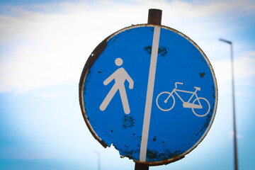 Cartello stradale rotondo blu, arrugginito, che indica una pista ciclabile divisa con i pedoni - obrazy, fototapety, plakaty