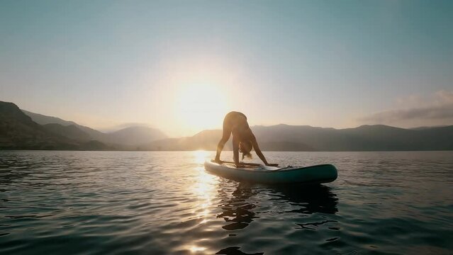 Young woman doing yoga on SUP board at sunset in slow motion