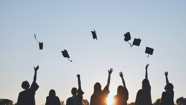 Silhouettes of Happy college graduates tossing their caps up at sunset.