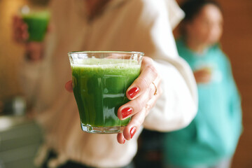 Woman proposing glass with green lymph tonic vitamin booster drink, close up image