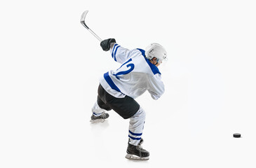 Young man, hockey player in motion during game, hitting puck with stick against white studio...