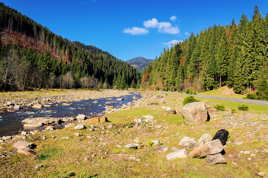 scenery with stones and rocks on the shore of a river. autumnal landscape in mountains with forested hills on a sunny day