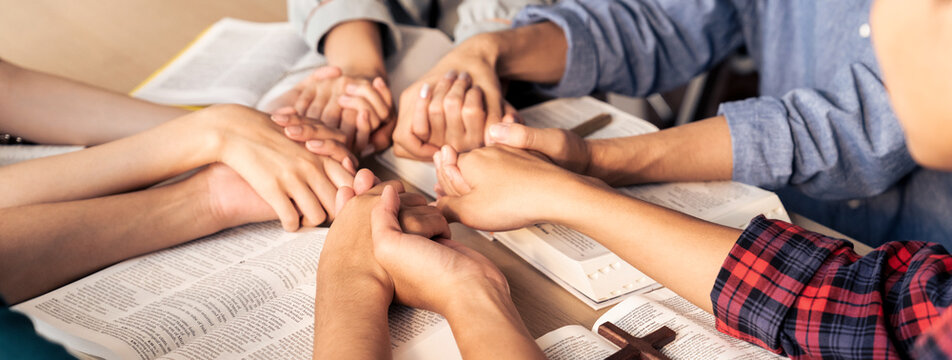 Cropped image of diversity people hand praying together at wooden church on bible book while hold hand together with believe. Concept of hope, religion, faith, god blessing concept. Burgeoning.