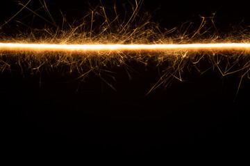 Burning gold sparkler straight line on black background as pattern. Christmas festive abstract...