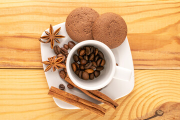Chocolate cookies, cinnamon, star anise, coffee beans on a ceramic saucer with a cup on a wooden table, macro, top view.