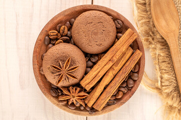 Chocolate cookies, cinnamon, star anise, coffee beans on a ceramic saucer with a cup on a wooden table, macro, top view.