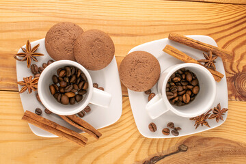 Chocolate cookies, cinnamon, star anise, coffee beans on a ceramic saucer with a cup on a wooden table, macro, top view.
