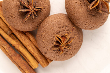 Three chocolate cookies with cinnamon sticks and star anise on a ceramic dish, macro, top view.