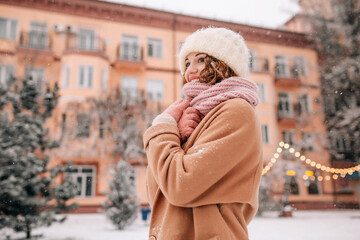 A middle-aged woman enjoys the snow against the backdrop of a winter city and Christmas lights on a pleasant January snowy day.