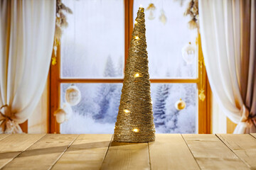 Wooden retro yellow table and blurred background of window sill. Christmas tree and empty space for your decoration. Natural light and magic time. Mockup background and cold december time.