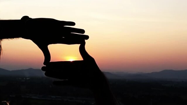 The man making frame round the sun with her hands in sunrise,Future planning idea 2024 concept,
Travel freedom a concept, Close up of traveler man hands making frame gesture with sunset in summer