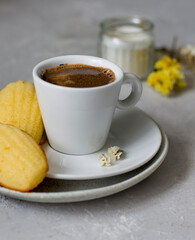 A small cup of espresso with a biscuit, a candle on a light gray background.