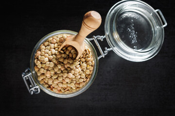 Uncooked lentil legumes in jar on black table. Top view.