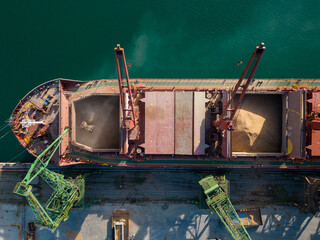 Aerial view of big cargo ship bulk carrier is loaded with grain of wheat in port at sunset