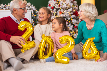 Grandparents celebrating New Year with granddaughters holding 2024 balloons
