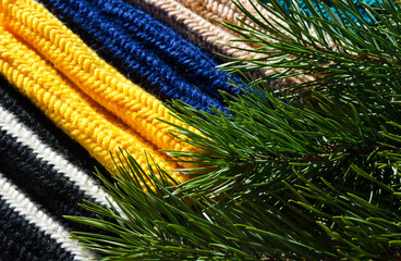 Mittens and three balls of wool yarn on a background of a green Christmas tree.
