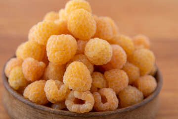 Yellow raspberries in a wooden bowl on the table. Summer berries background. Vitamin food, berry harvest. Healthy nutrition.