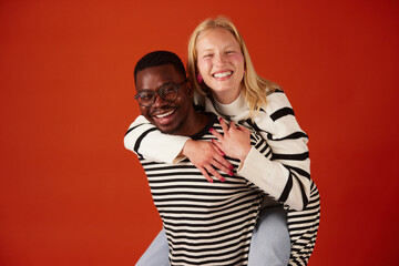 Joyful multiracial couple having fun together piggybacking over orange background