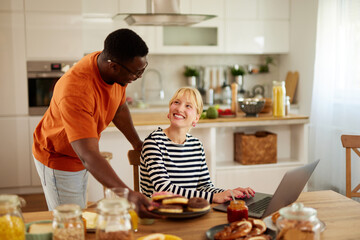 Young multiracial couple talking and using a laptop over breakfast at home