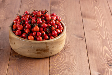 red dog-rose rosehip fruits in a wooden bowl on wooden table