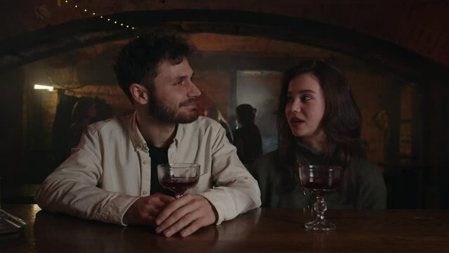 Caucasian woman meets with handsome guy at bar. Girlfriend saying toast to her best friend in pub. Couple drinking alcohol cocktails together. Positive conversation of two strangers