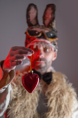 comic hare man, young guy in cringe in scary rabbit mask looks at heart, concept murderous love,...