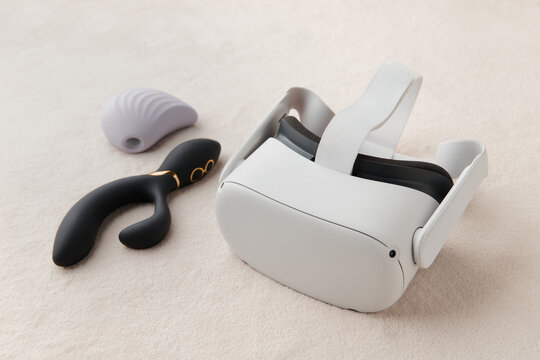 Purple clitoral vibrator, black dildo and virtual reality goggles on the white fur background